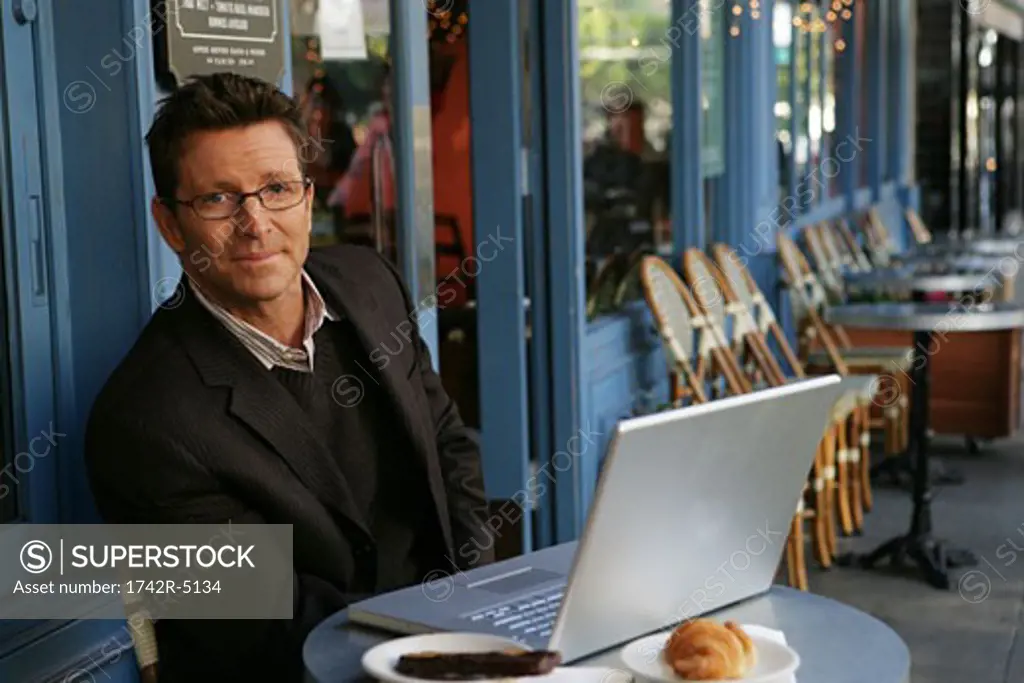 Mature man sitting at an outdoor cafe with a laptop