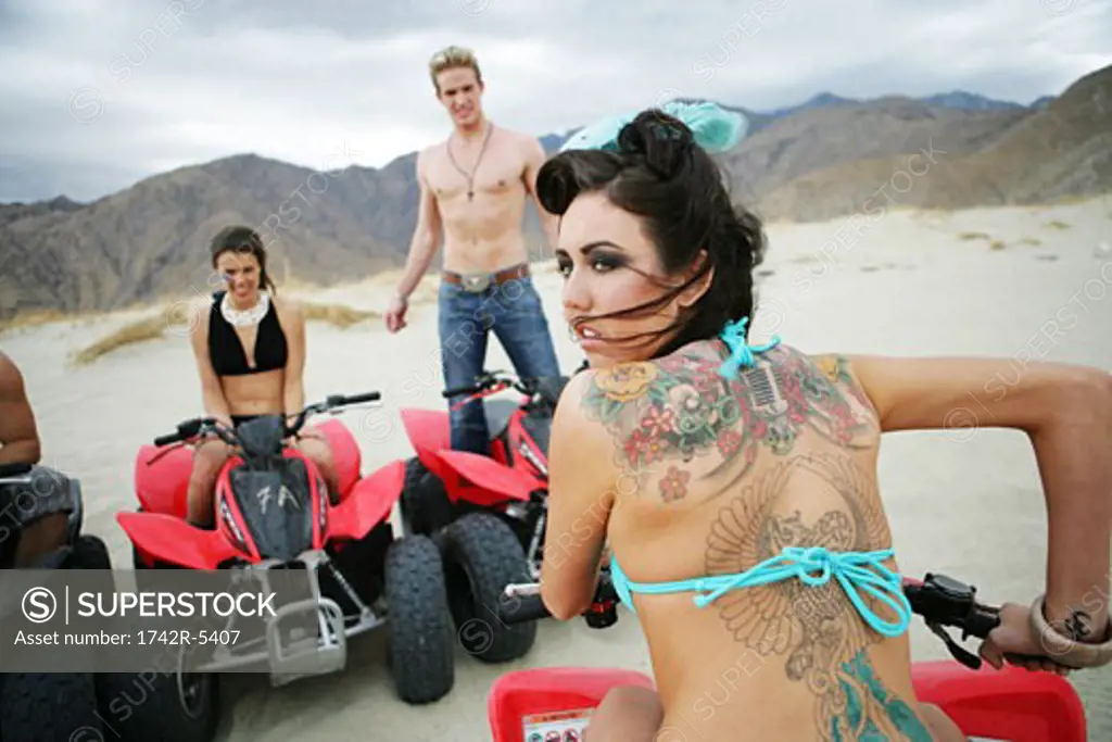 Young woman with tattoos riding ATV, friends behind