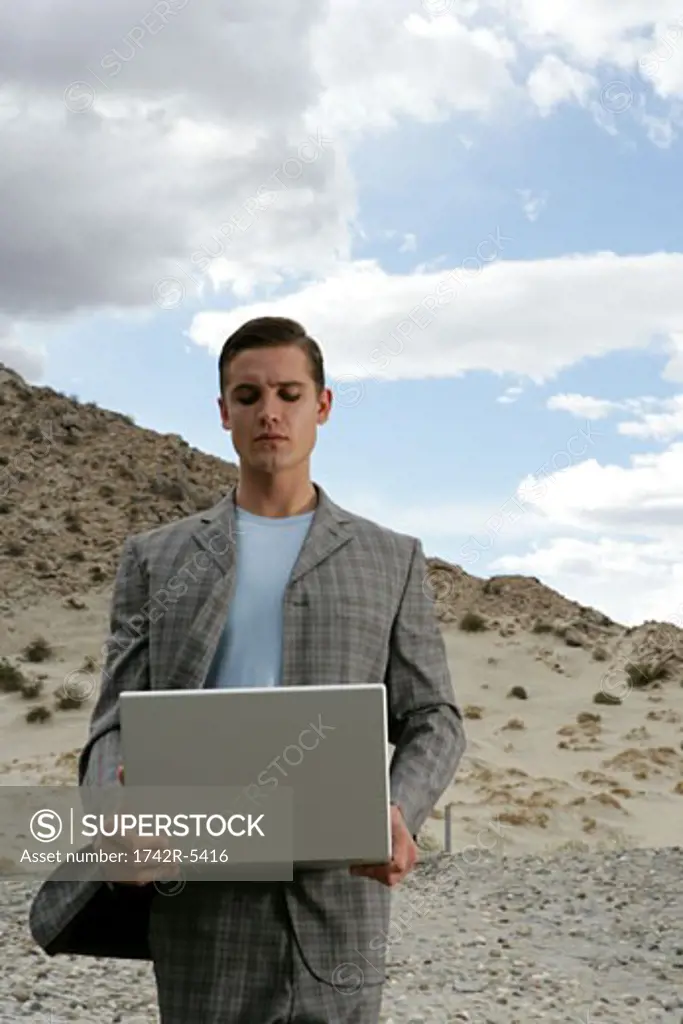 Man standing in desert, holding a laptop