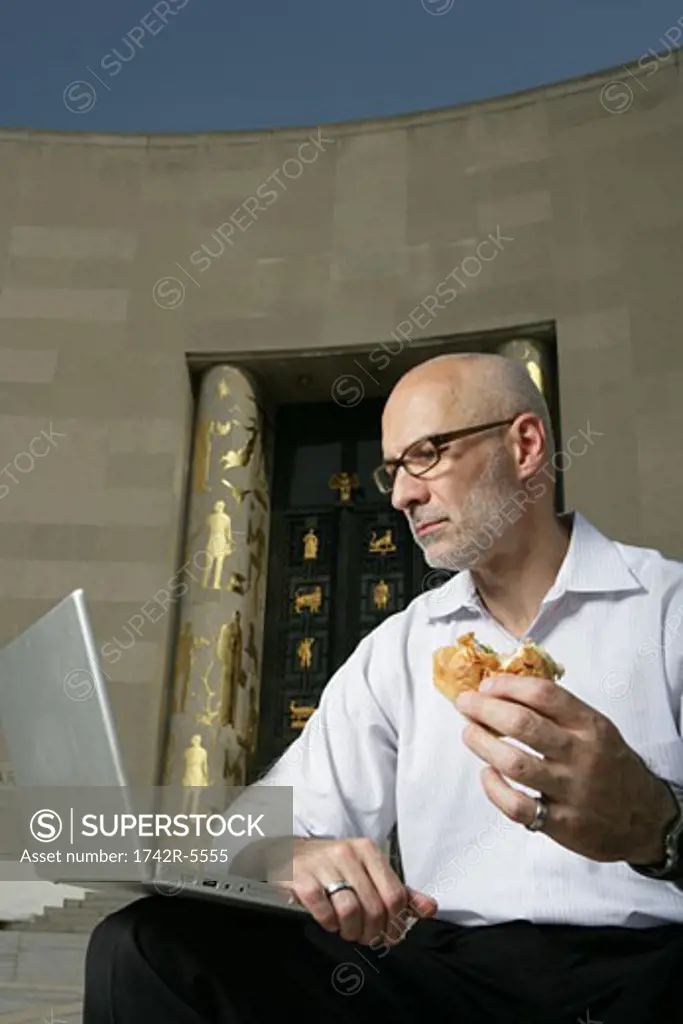 mature man working on laptop eating lunch