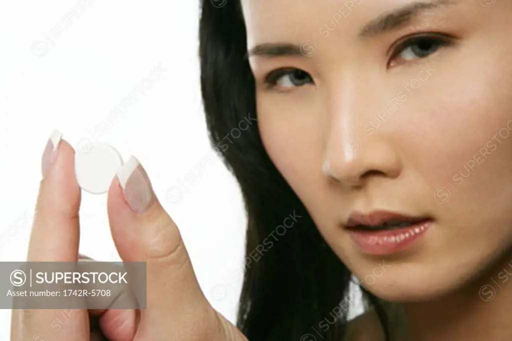 Asian woman holding a pill, looking at camera