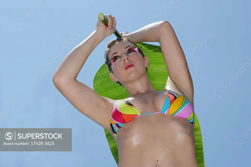 Woman wearing a bikini holding a large palm leaf