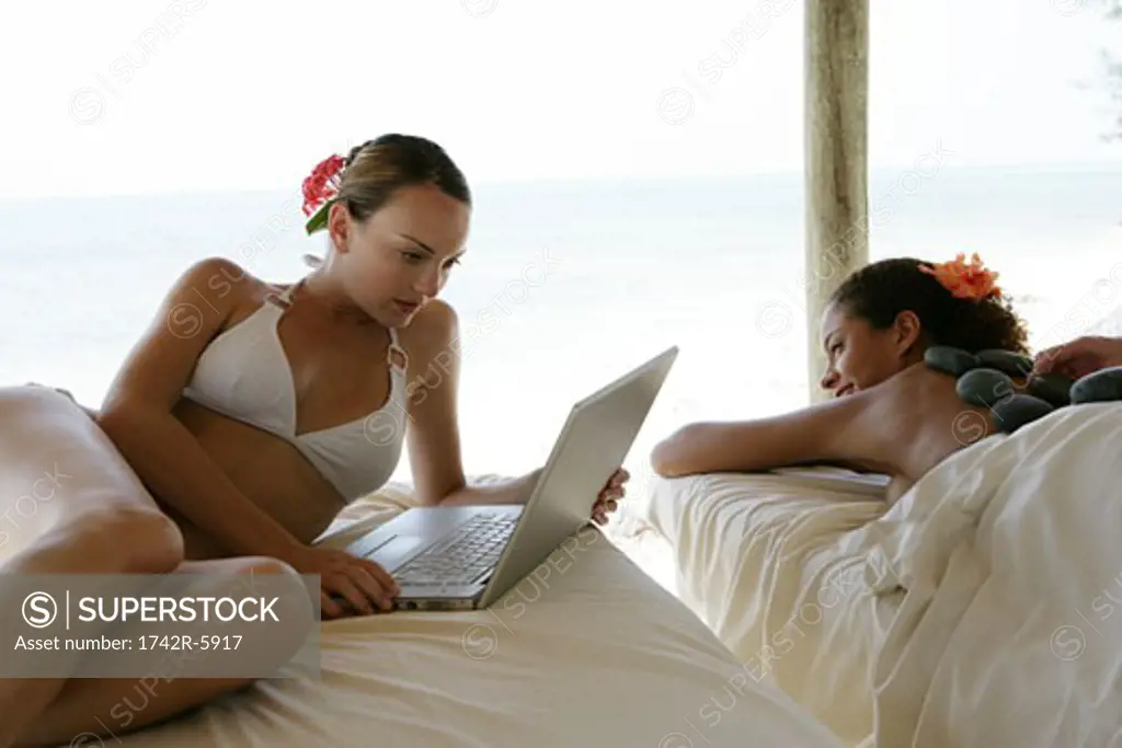 Young women using laptop and getting massage at beach.