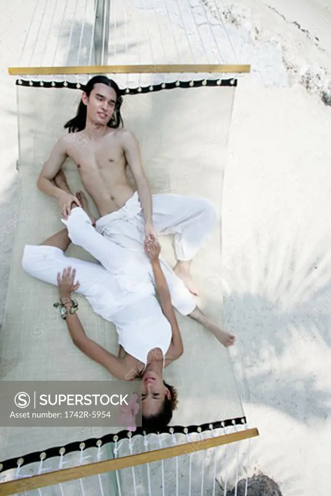 Young couple relaxing in hammock on beach.