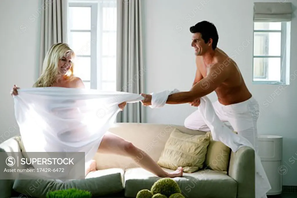 Young man pulling sheet of nude woman.