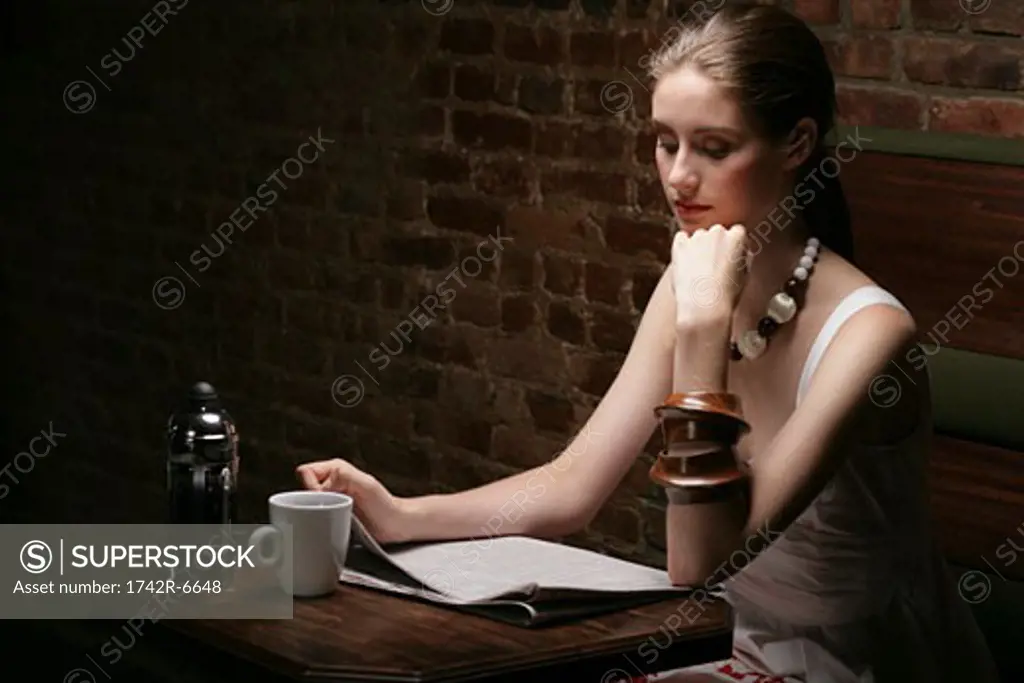 Young stylish woman reading newspaper in cafe.