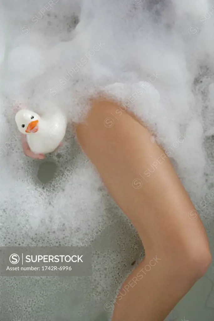 Detail of woman's leg in bubble bath with rubber duck.