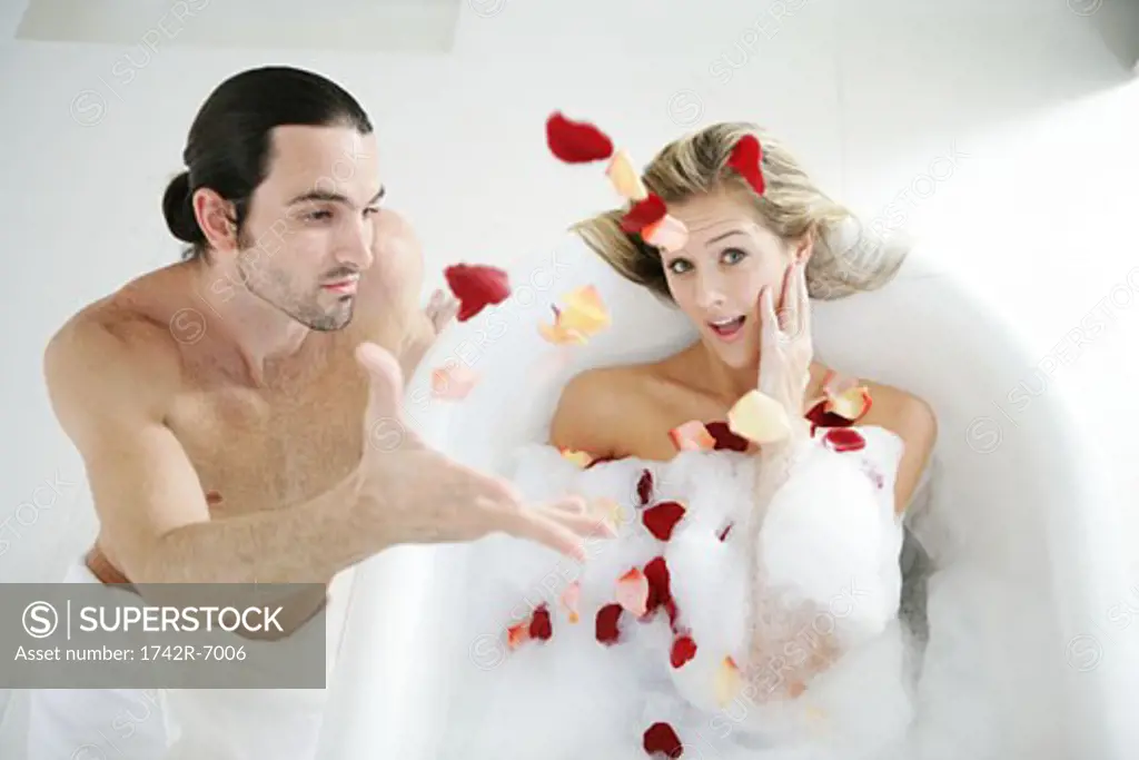 Young man throwing rose petals in woman's bubble bath.