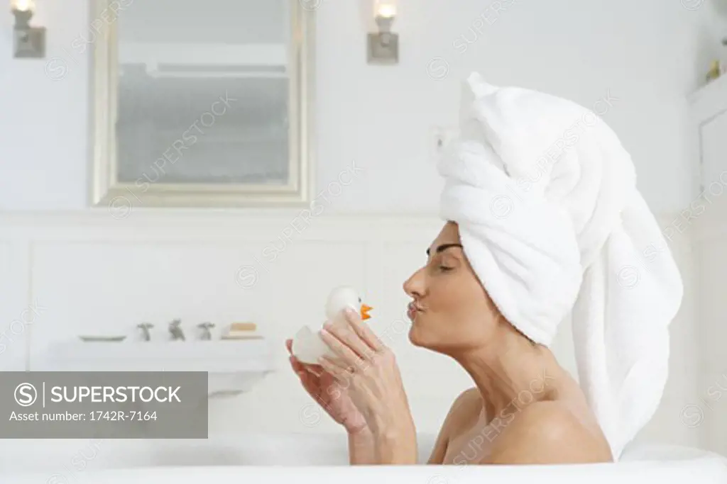 Woman in bathtub kissing rubber duck.