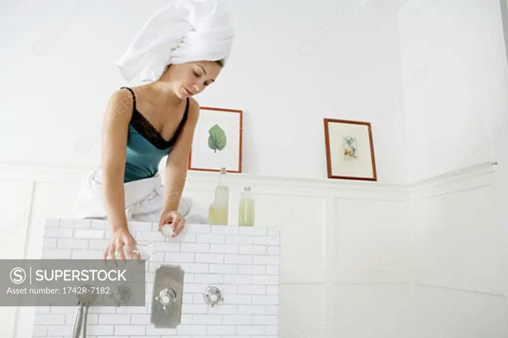 Young woman pouring oil in bath.