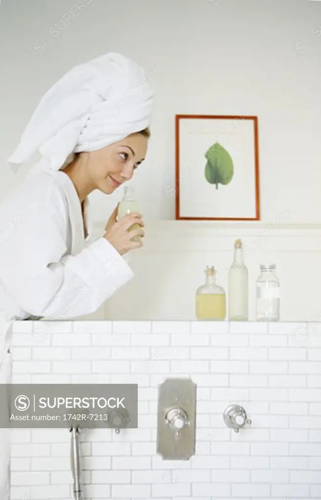 Young woman smelling bath oil in bathroom.