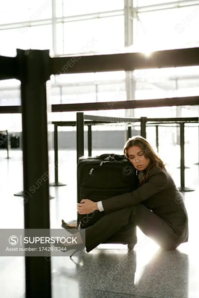 Tired businesswoman hugging luggage in airport.