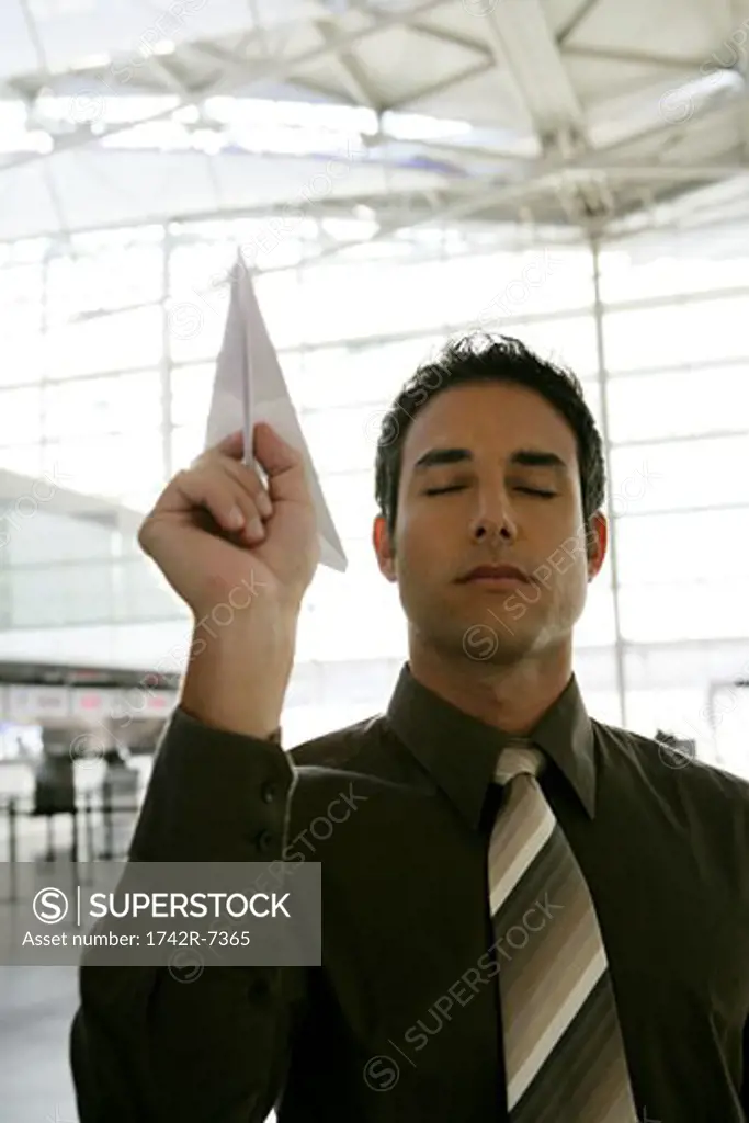 Young businessman throwing paper airplane in airport.