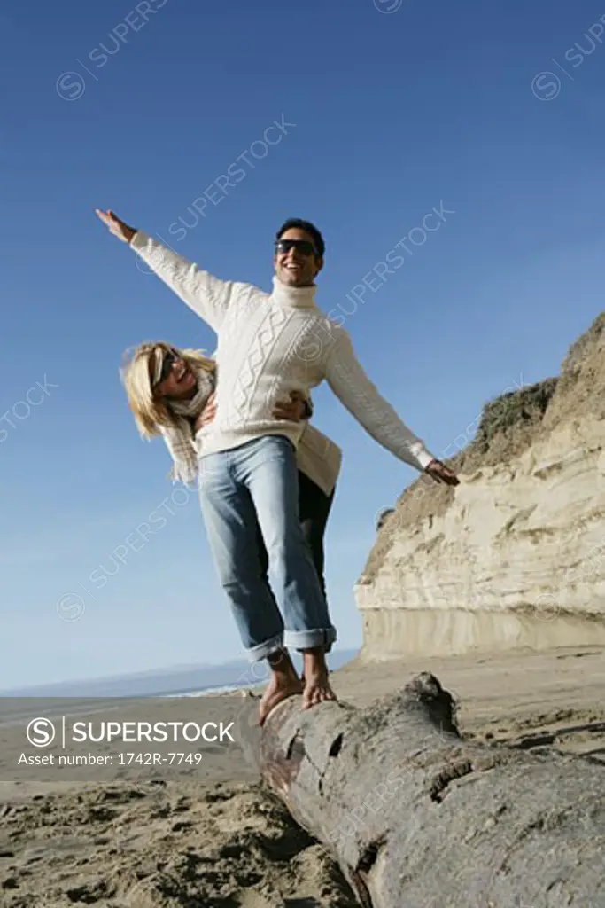Young couple balancing on log at beach.