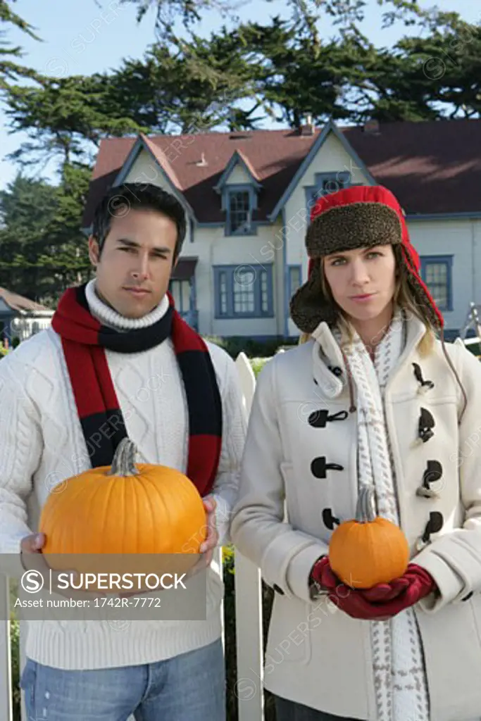 Young couple holding pumpkins outdoors.