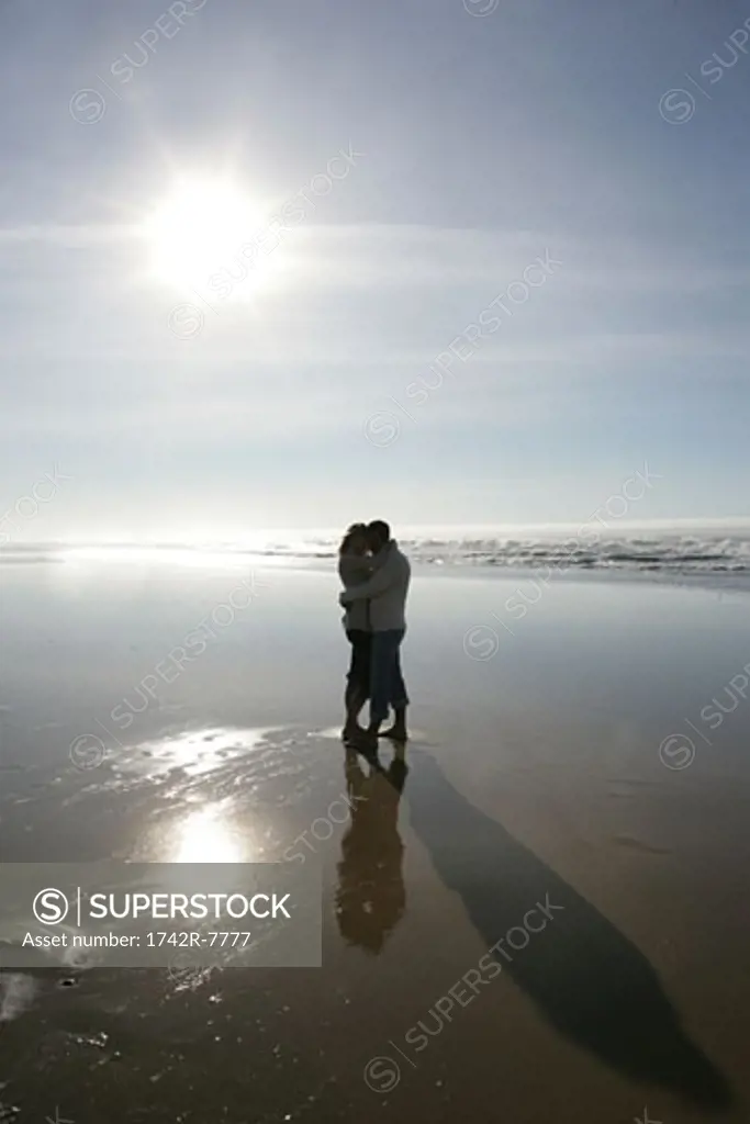 Silouhette of couple hugging on beach.