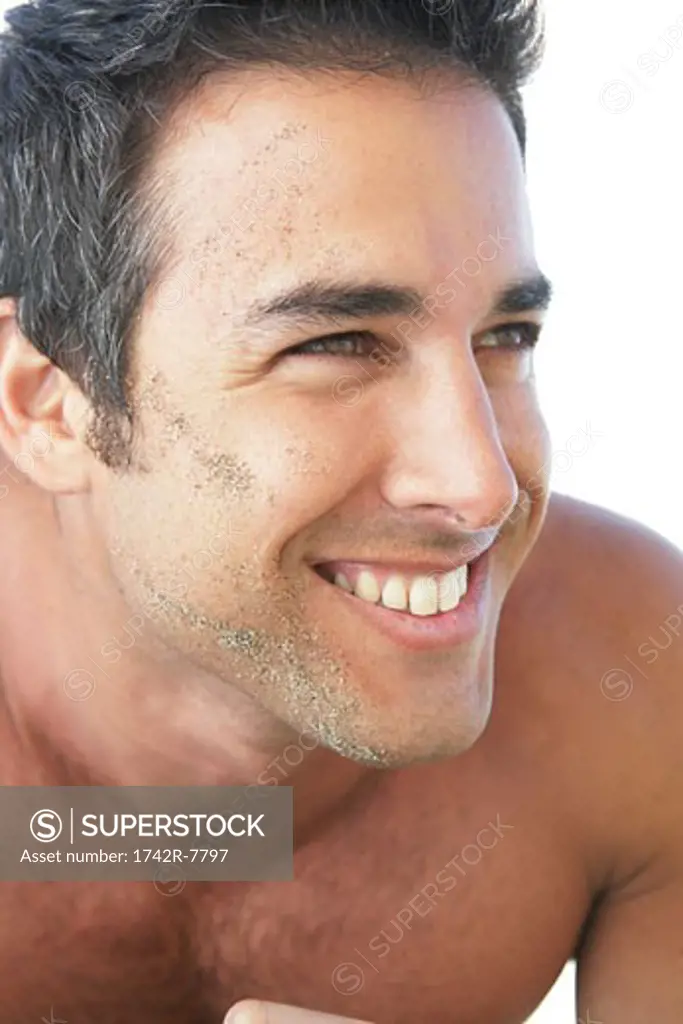 Happy young bare-chested man with sand on face.