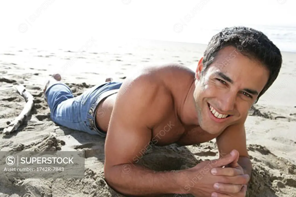 Young bare-chested man relaxing on beach.