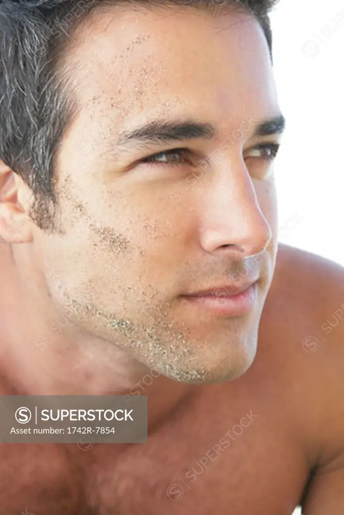 Young bare-chested man with sand on face.
