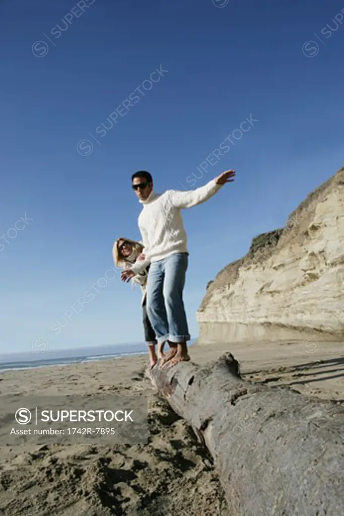 Young couple balancing on log at beach.
