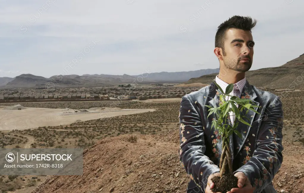 Young man holding a plant in a desert