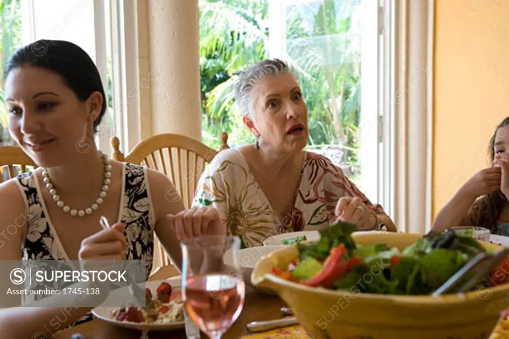 Senior woman sitting at a dining table with her daughter and granddaughter
