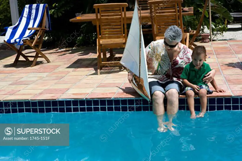 Senior woman holding a sailboat with her grandson at poolside