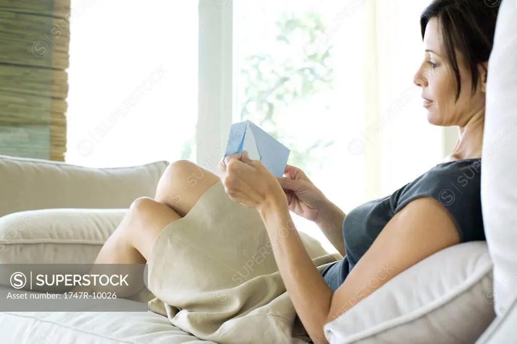Woman sitting on sofa, removing letter from envelope