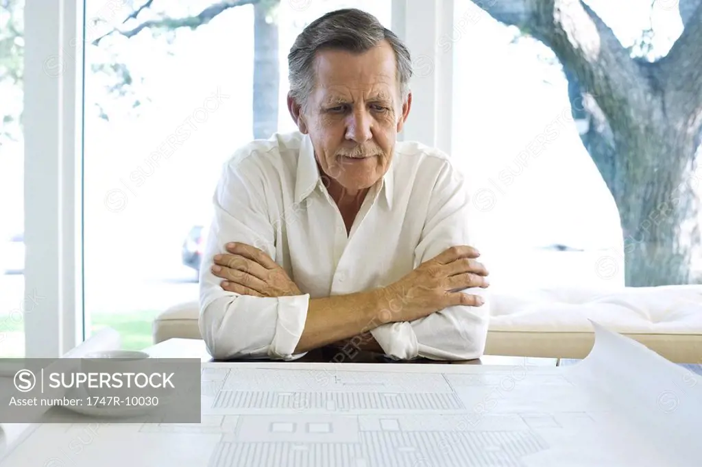 Man looking at blueprint, coffee cup nearby