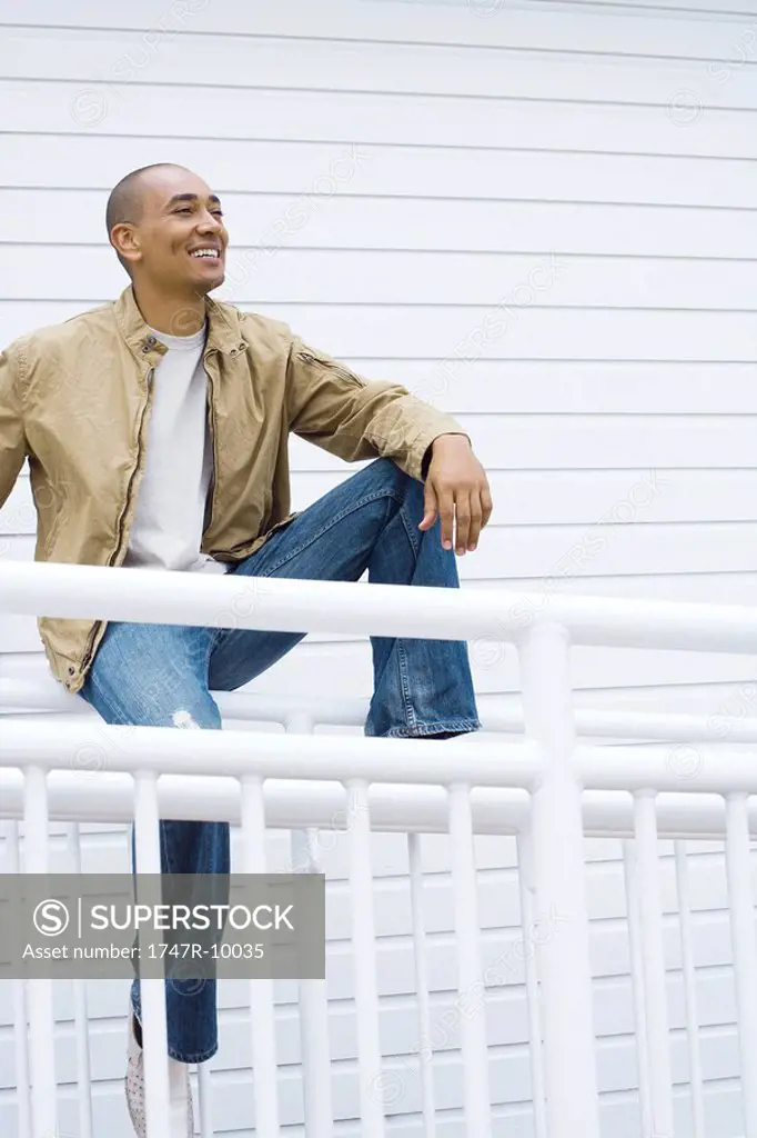 Man sitting on railing, looking away, smiling