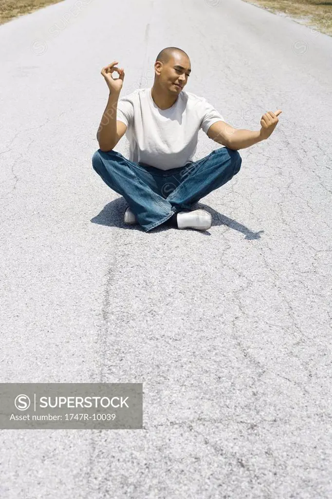 Hitchhiker sitting in the middle of the road in lotus position, holding one thumb out