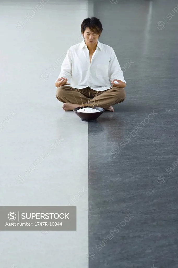 Man sitting in lotus position with bowl of incense