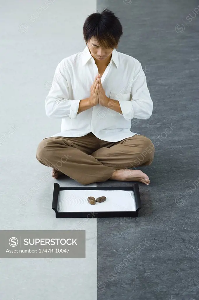 Man sitting in front of rock garden in lotus position, hands clasped