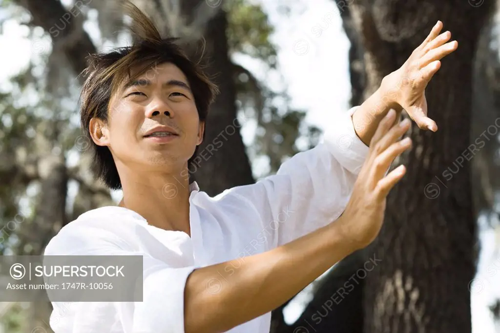 Man standing outdoors with hands raised, hair tousled by breeze, low angle view