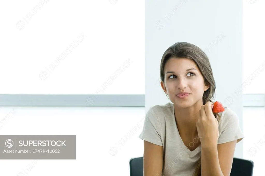 Teen girl holding strawberry, looking away