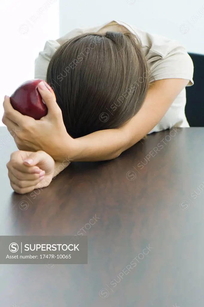 Teen girl holding apple, head resting on arms