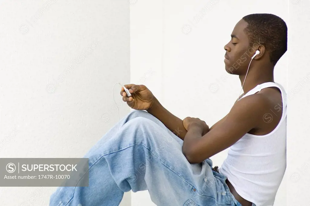Teen boy sitting, listening to MP3 player, side view