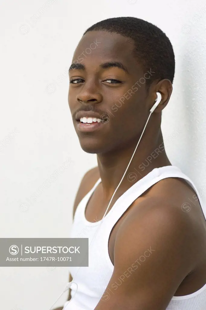 Teen boy listening to earphones, smiling at camera, portrait