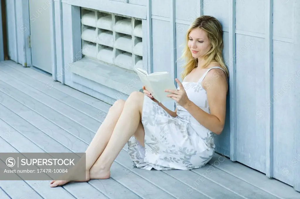 Young woman sitting on deck, reading book