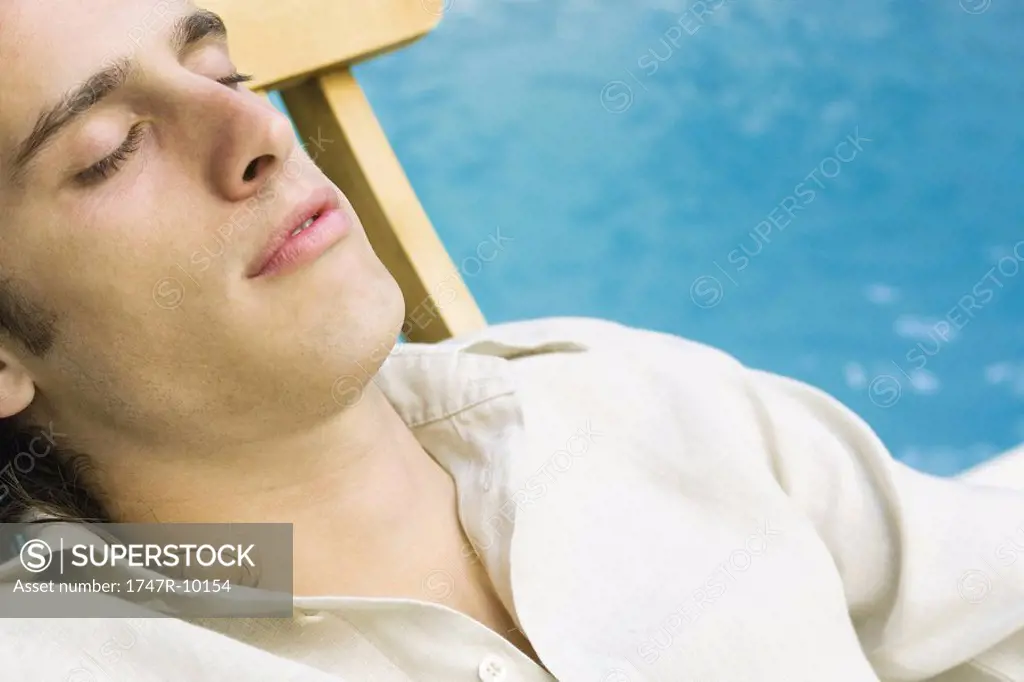 Man reclining in lounge chair beside pool, eyes closed, close-up