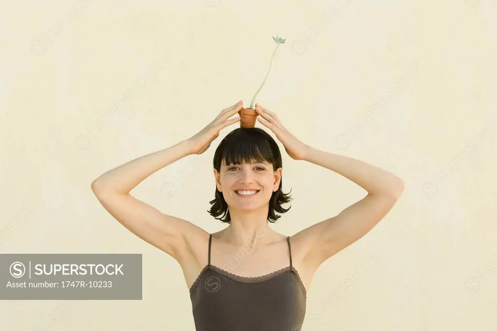 Woman holding small potted plant on head, smiling at camera, portrait