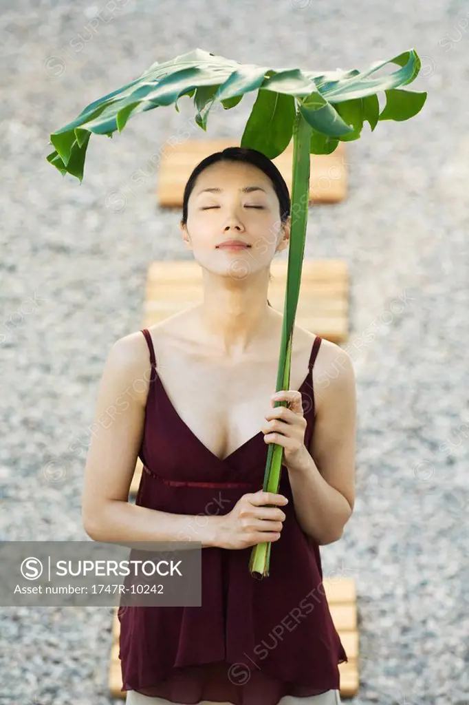 Woman holding palm leaf over her head, eyes closed, smiling