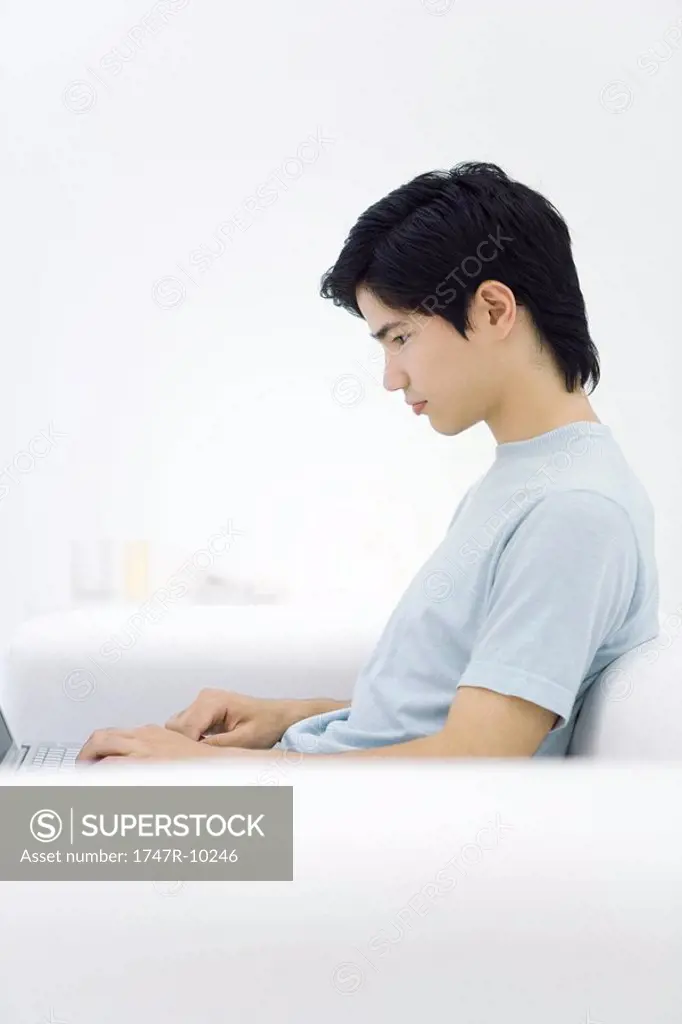 Young male sitting on sofa, using laptop, side view