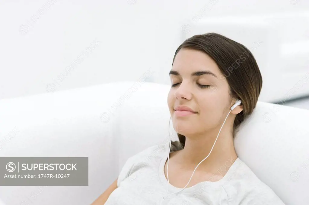 Female reclining on sofa, listening to earphones, eyes closed