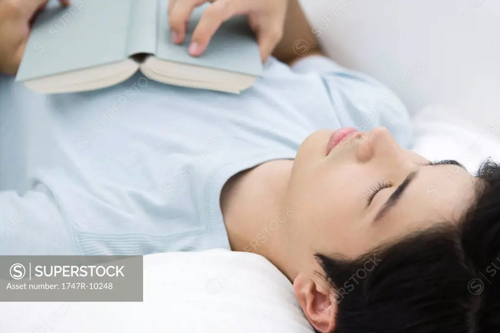 Young male lying on back with eyes closed, holding book on chest