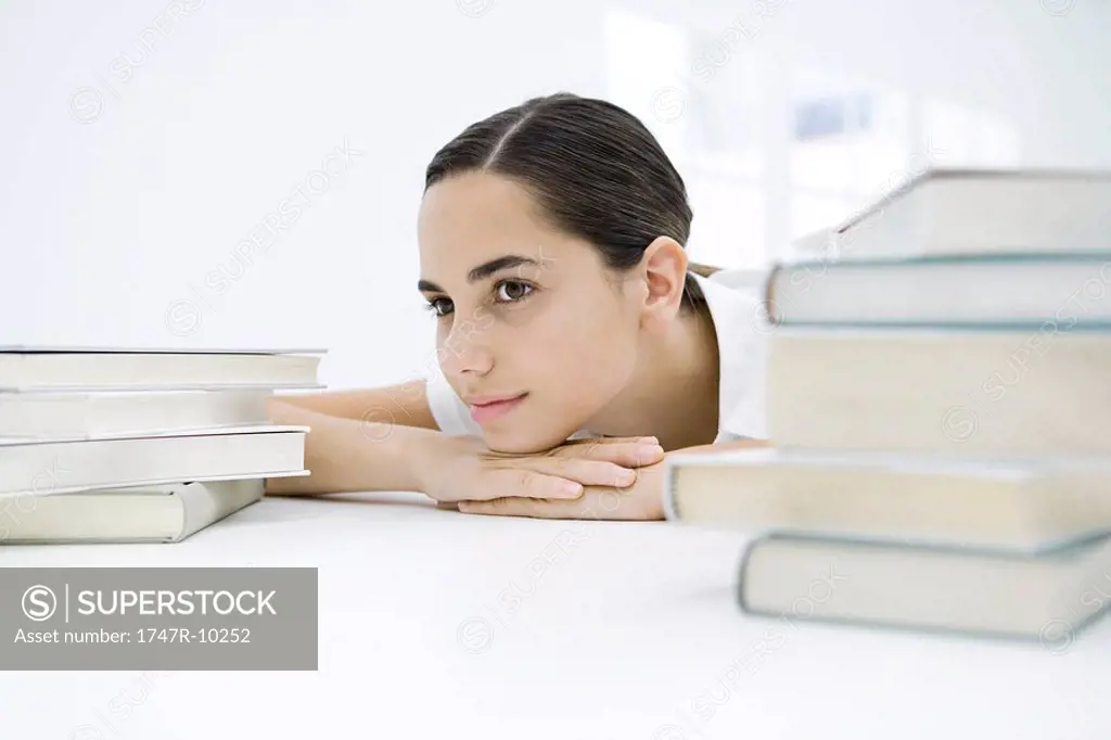Female student between two stacks of books, head resting on arms, looking away