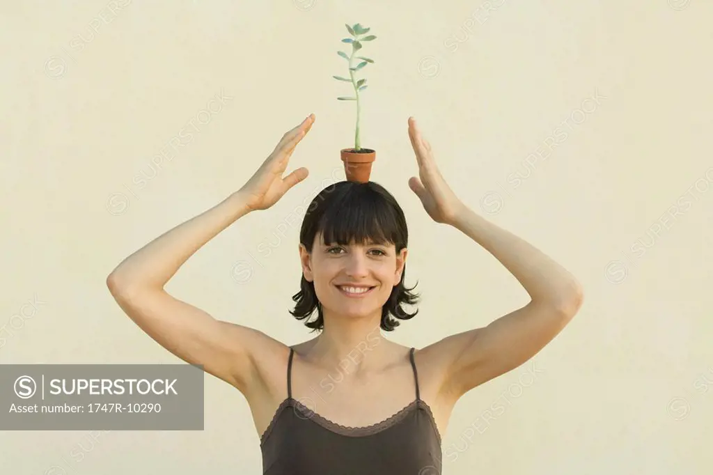 Woman balancing small potted plant on head, smiling at camera, portrait
