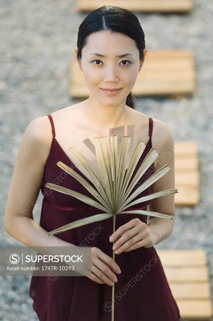 Woman holding dried palm leaf, smiling at camera