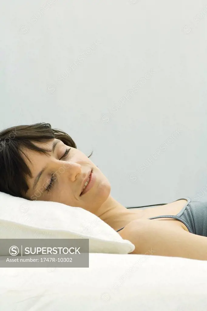 Woman lying on pillow, smiling, eyes closed