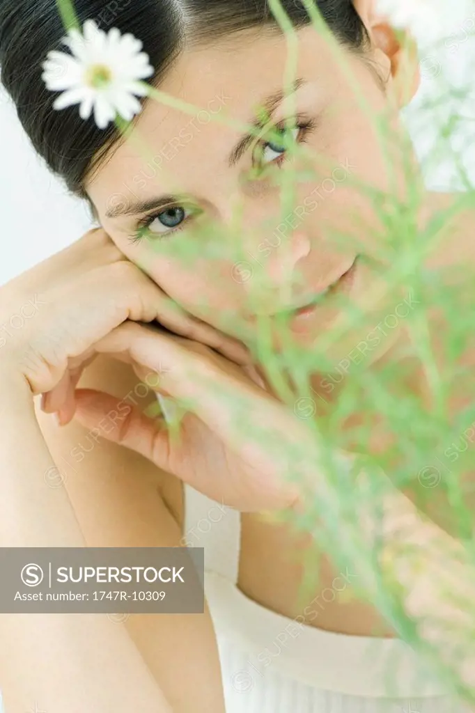 Woman behind chamomile plant, smiling at camera, portrait